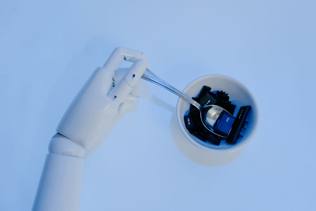 A robotic hand holds a spoon filled with keyboard keys, symbolizing AI and technology fusion