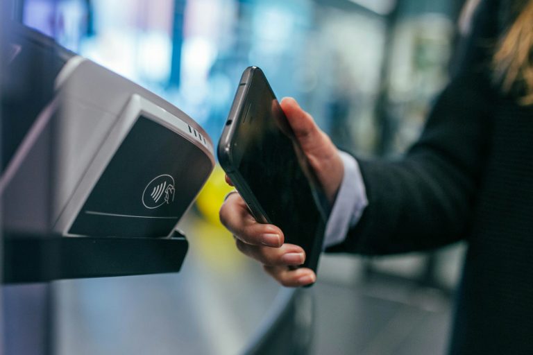 A person holds a smartphone beside a contactless payment reader