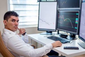 Professional stock market analyst monitoring data on multiple screens at a workstation