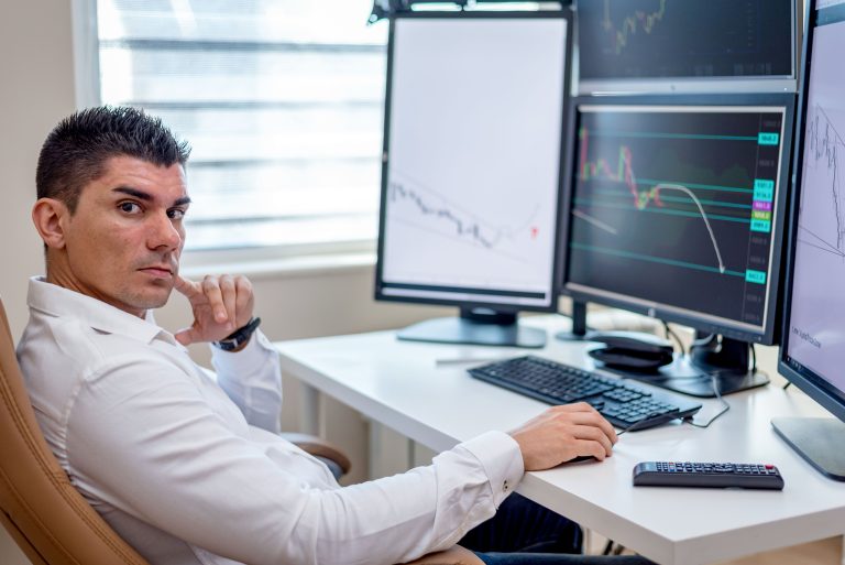 Professional stock market analyst monitoring data on multiple screens at a workstation
